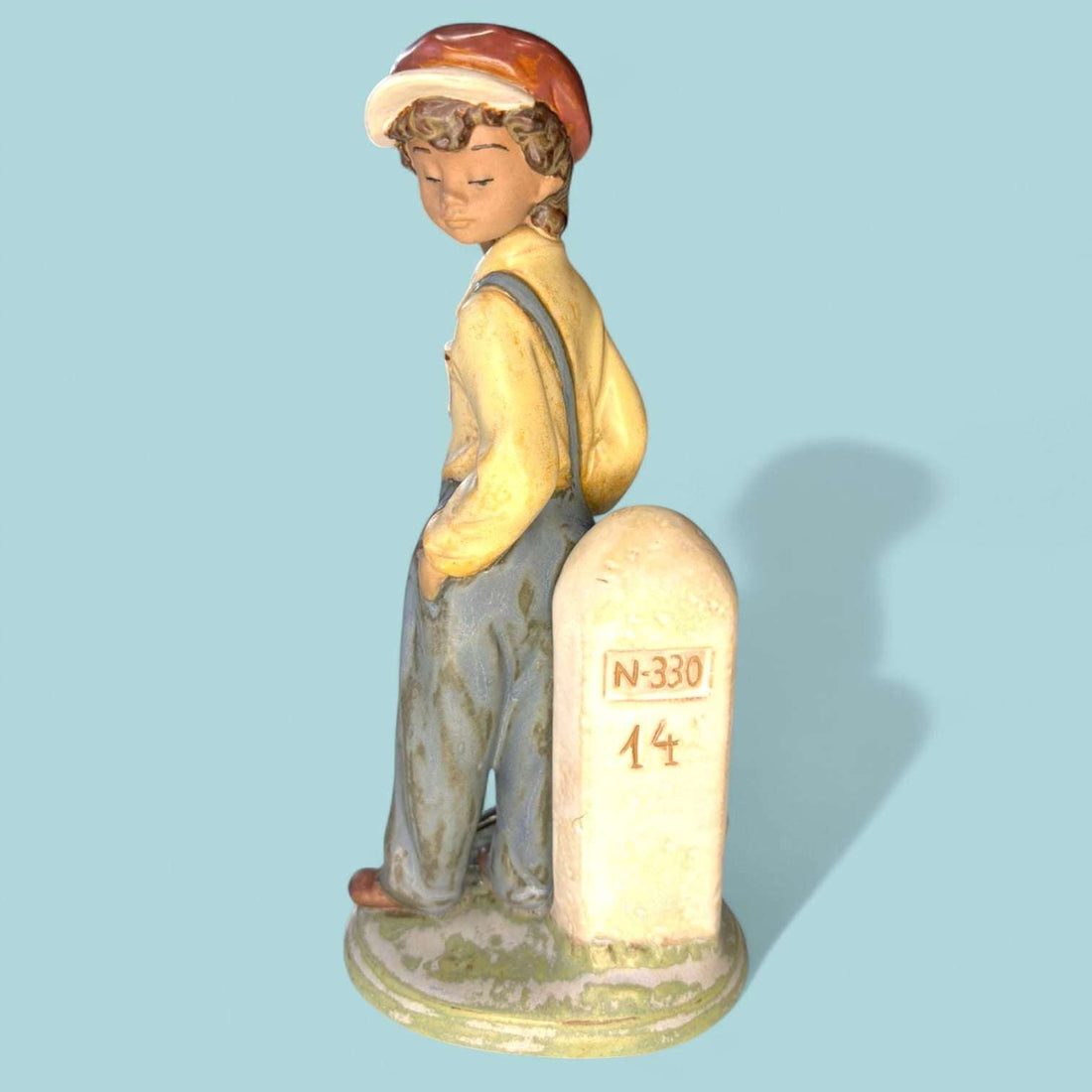 La figura “Niño Viajero” (Wanderer Boy) de Lladró representa a un joven caminante apoyado en un hito de carretera marcado con la inscripción “N-330”, evocando el espíritu aventurero, la nostalgia de los viajes y la sencillez de la vida rural.

