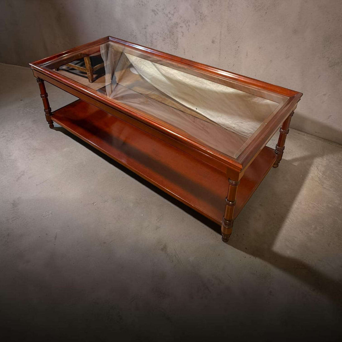Esta Mesa baja de caoba con tapa de cristal es una pieza pensada para aportar calidez, orden y distinción al salón.