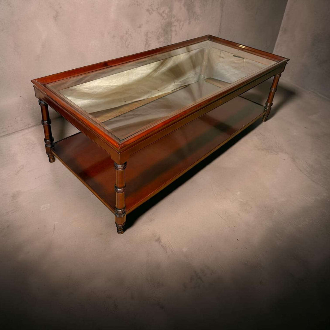 Esta Mesa baja de caoba con tapa de cristal es una pieza pensada para aportar calidez, orden y distinción al salón.