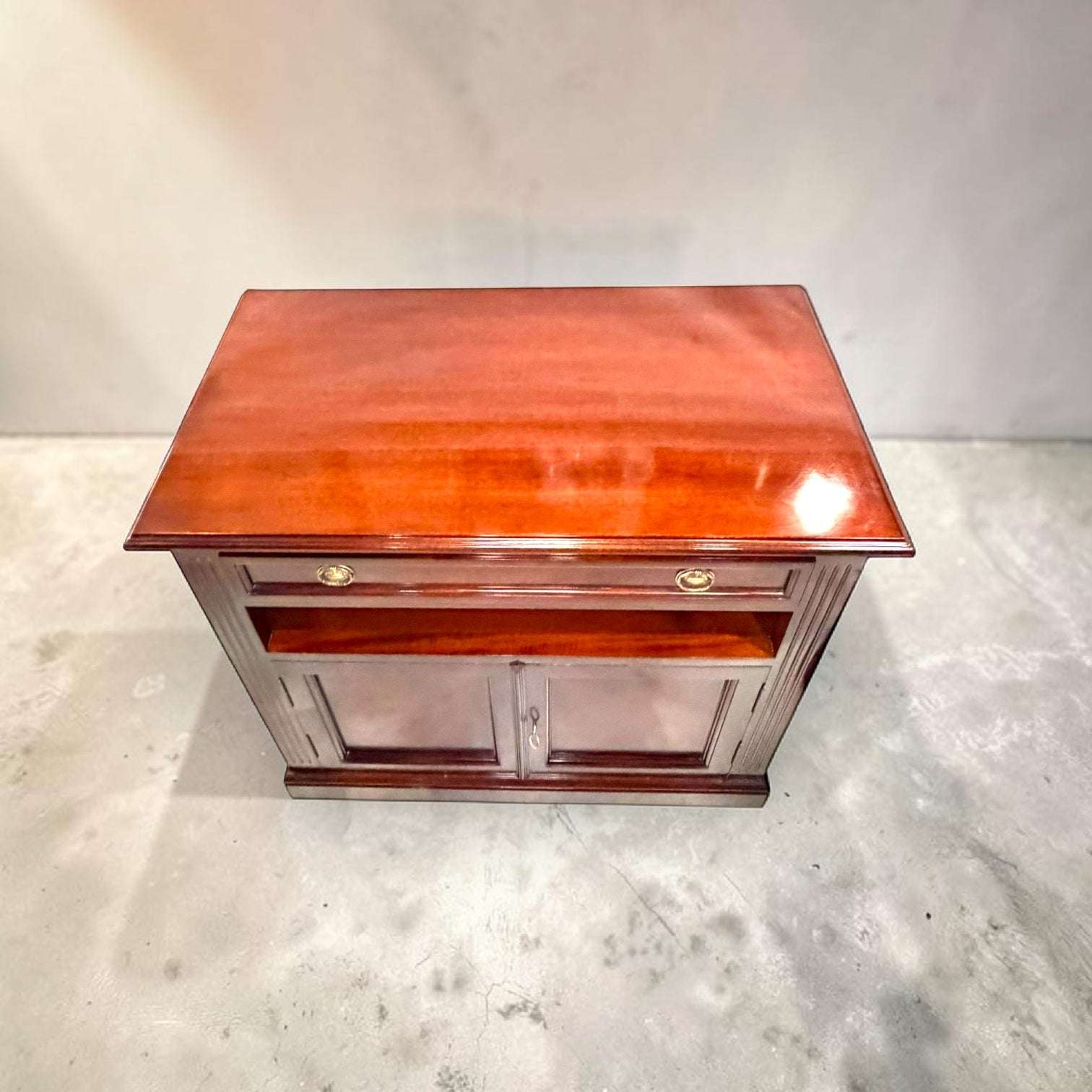 El diseño combina utilidad y estilo: en la parte superior cuenta con una amplia superficie rectangular, debajo incorpora un cajón frontal y en la zona inferior dispone de una alacena con puertas y llave. 