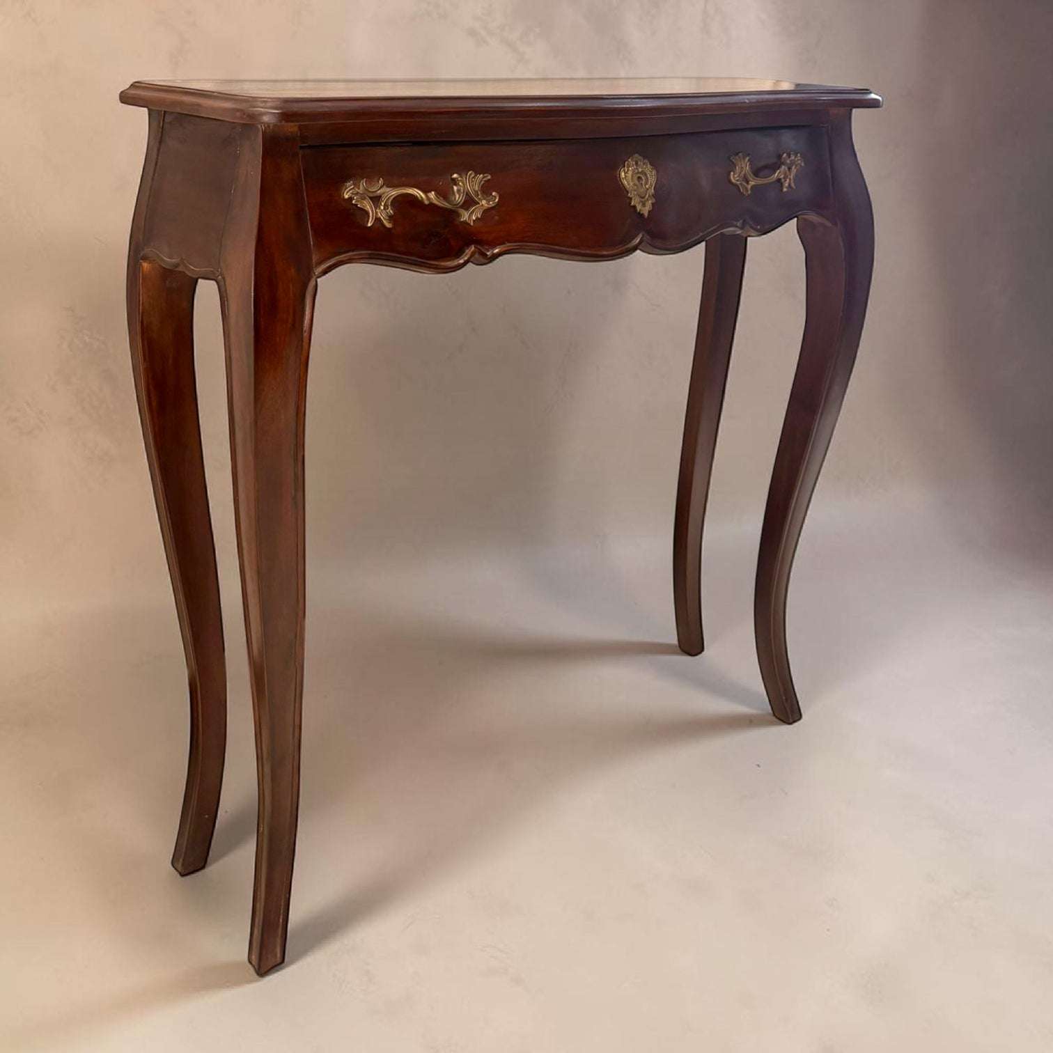 
Destacan especialmente sus patas curvas de estilo cabriolé, su faldón frontal ondulado, el acabado pulido de la madera y la elegancia de sus herrajes metálicos. El cajón frontal perm