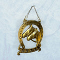 Este Colgador de llaves destaca por su acabado dorado envejecido, su forma de herradura y su composición central con dos caballos en relieve. 