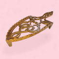 Este Descansadero destaca por su diseño calado, elegante y ornamental. Su estructura presenta formas curvas, motivos simétricos y una silueta alargada que recuerda a los antiguos soportes domésticos utilizados en tareas de planchado. 