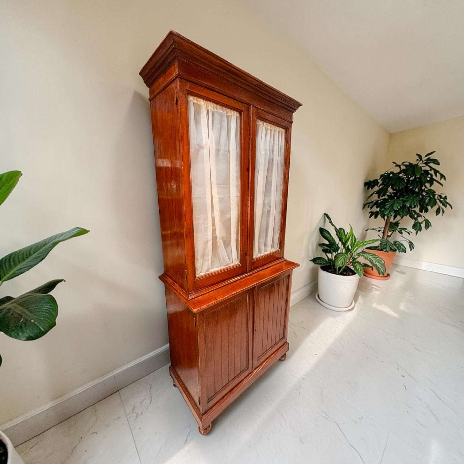  La parte superior cuenta con dos puertas acristaladas enmarcadas en madera, con cortinas claras que permiten ocultar parcialmente el interior y crear una imagen más delicada.