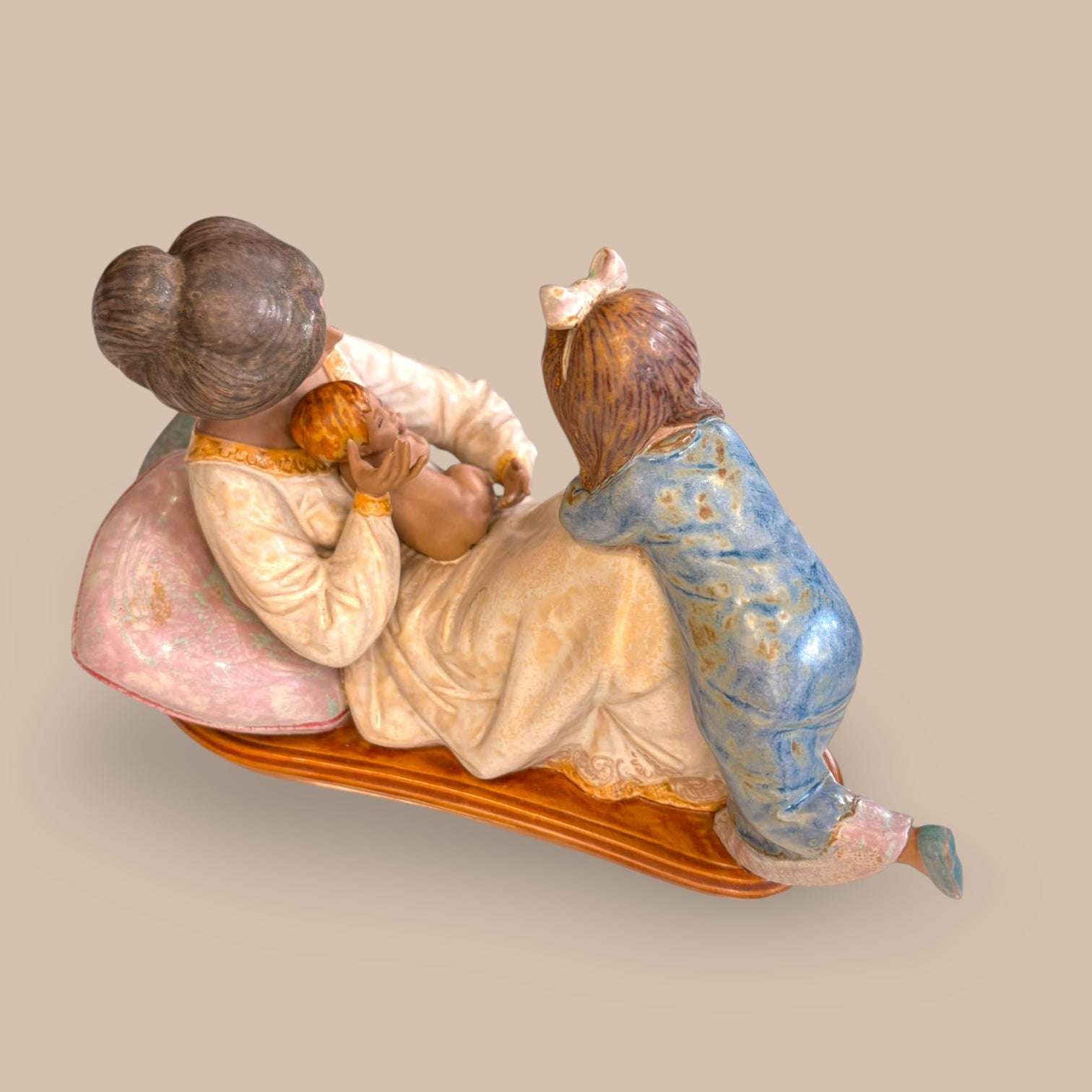  La escena recoge uno de esos momentos íntimos que conectan con la memoria familiar, con la infancia y con el valor de las piezas que cuentan una historia sin necesidad de palabras. La madre aparece recostada, vestida en tonos claros, sosteniendo al bebé mientras la hija mayor se acerca sobre la cama, creando una composición equilibrada, dulce y muy decorativa.

El sello de Lladró en la base refuerza su interés para coleccionistas y amantes d