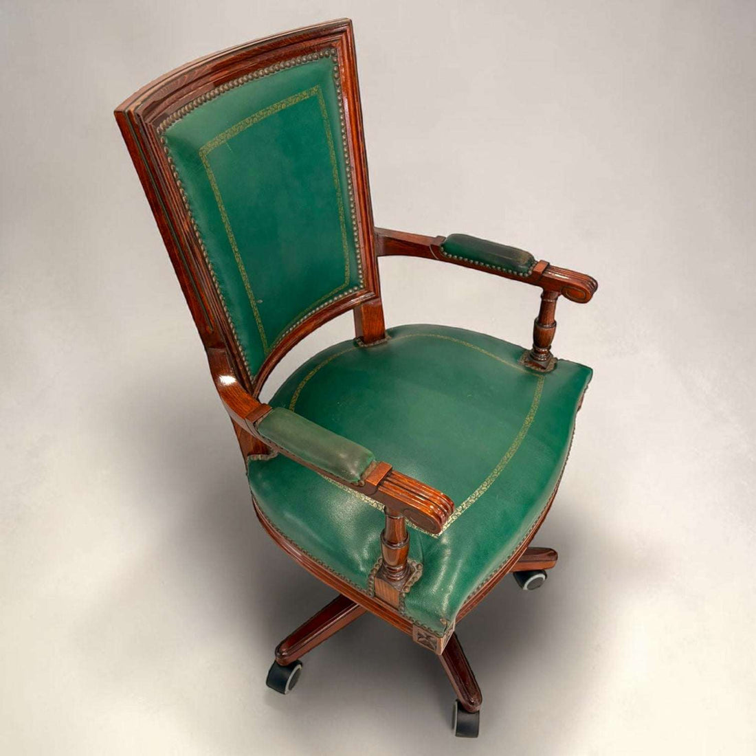 El sillón presenta asiento amplio tapizado, respaldo alto con panel verde, reposabrazos tapizados y estructura de caoba con vetas cálidas. 
