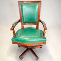 El sillón presenta asiento amplio tapizado, respaldo alto con panel verde, reposabrazos tapizados y estructura de caoba con vetas cálidas. 