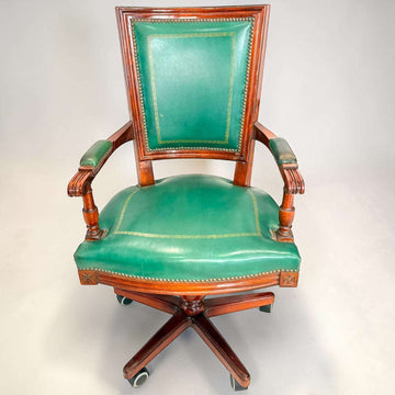 El sillón presenta asiento amplio tapizado, respaldo alto con panel verde, reposabrazos tapizados y estructura de caoba con vetas cálidas. 