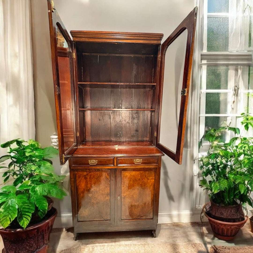  La parte superior cuenta con dos puertas de cristal enmarcadas en madera, con formas suavemente arqueadas en la zona superior, lo que aporta un detalle elegante y distinguido. En el interior se aprecian estantes para colocar libros, copas, vajilla, porcelanas, figuras decorativas o piezas de colección.
