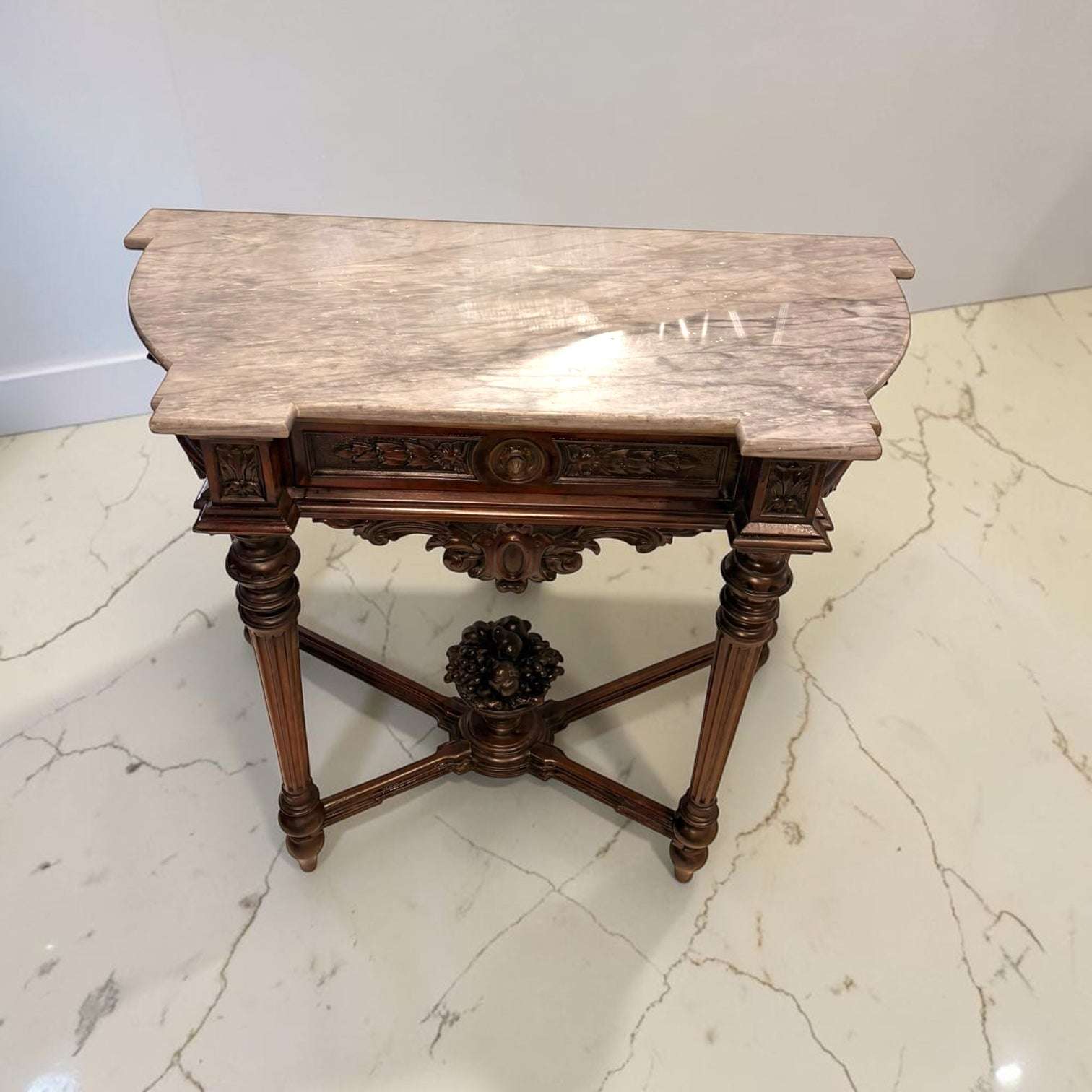 La tapa de mármol grisáceo aporta un punto de sofisticación difícil de encontrar hoy en muebles nuevos, mientras que la caoba tallada conserva ese acabado cálido, brillante y noble que solo tienen los muebles con historia.