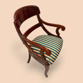 Este Sillón de estilo Biedermeier, datado alrededor de 1890, es una pieza antigua de gran elegancia, fabricada en madera de caoba y acompañada por un asiento tapizado a rayas en tonos verde azulado, dorado y crema.