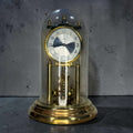 Reloj aniversario o reloj de péndulo de torsión marca Kundo, una pieza muy reconocible por su estructura de metal dorado, su mecanismo visible y su elegante cúpula de cristal.