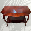 Mesa auxiliar de caoba con balda inferior, diseño clásico y elegantes líneas curvas. Una pieza funcional y decorativa, perfecta como mesa de apoyo en el salón, recibidor, dormitorio o junto a un sillón. 