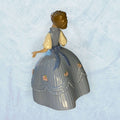 Su función principal es decorativa: embellecer vitrinas, aparadores, salones, dormitorios o espacios de colección donde se busque una pieza fina, luminosa y con presencia clásica.

La figura muestra a una niña de rostro sereno, con vestido azul de gran volumen, pliegues verticales muy marcados 