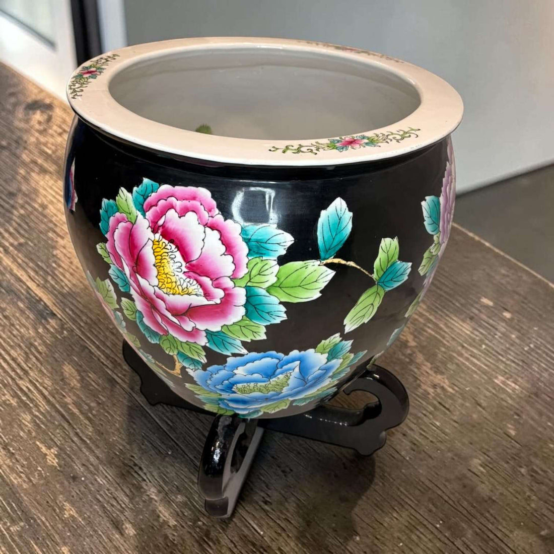 Jardinera china de porcelana negra con flores vibrantes en tonos rosa, azul y verde, decorada con soporte de madera, pieza decorativa oriental.