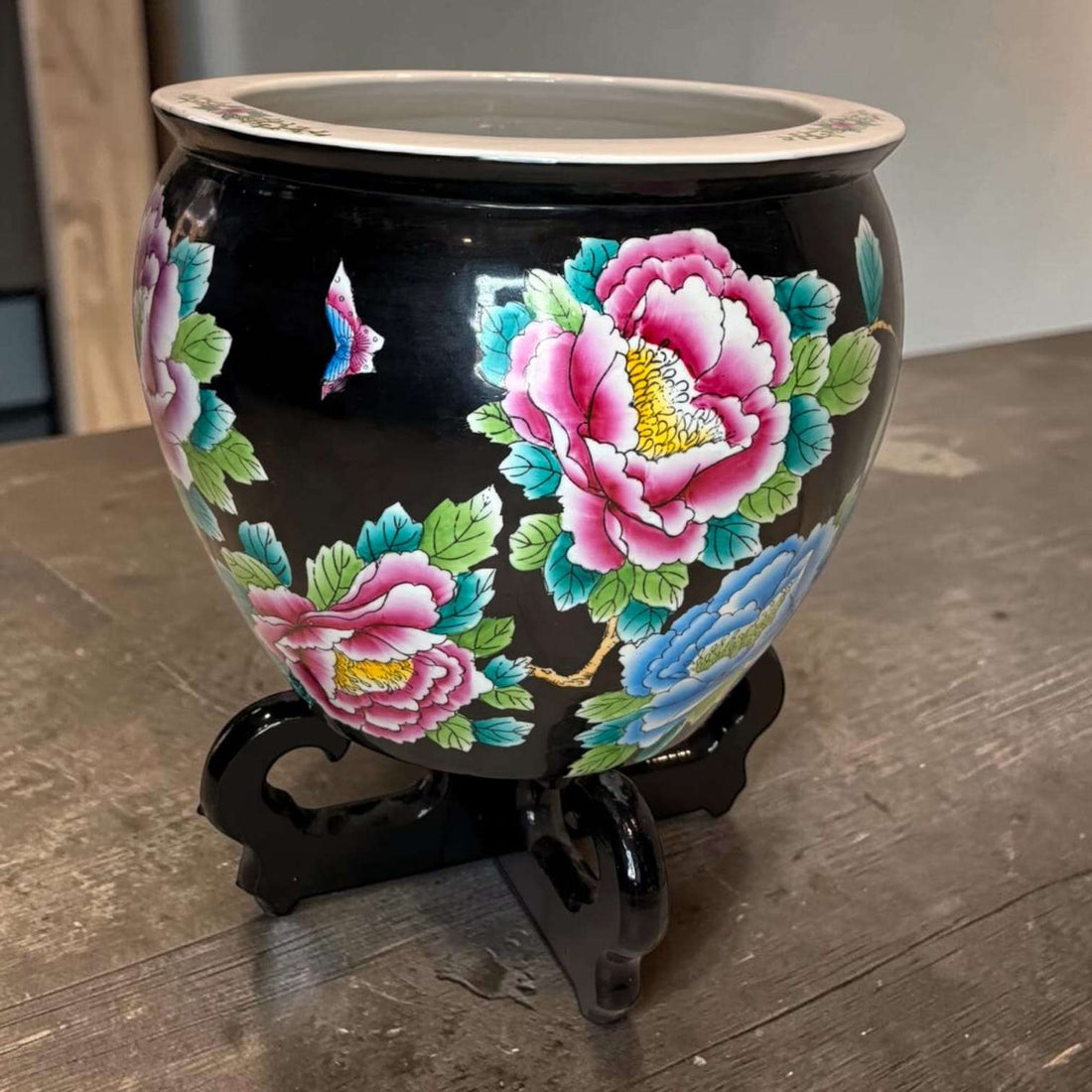 Jardinera china de porcelana negra con flores vibrantes en tonos rosa, azul y verde, decorada con soporte de madera, pieza decorativa oriental.
