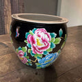 Jardinera china de porcelana negra con flores vibrantes en tonos rosa, azul y verde, decorada con estilo Famille Rose y soporte de madera