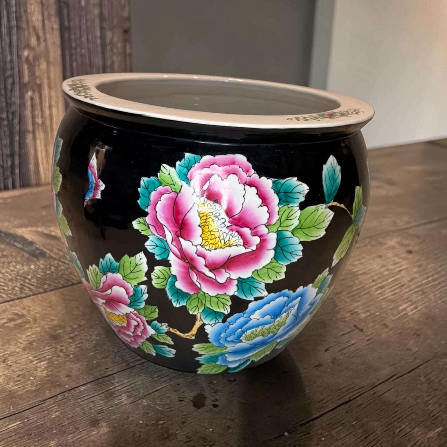 Jardinera china de porcelana negra con flores vibrantes en tonos rosa, azul y verde, decorada con estilo Famille Rose y soporte de madera