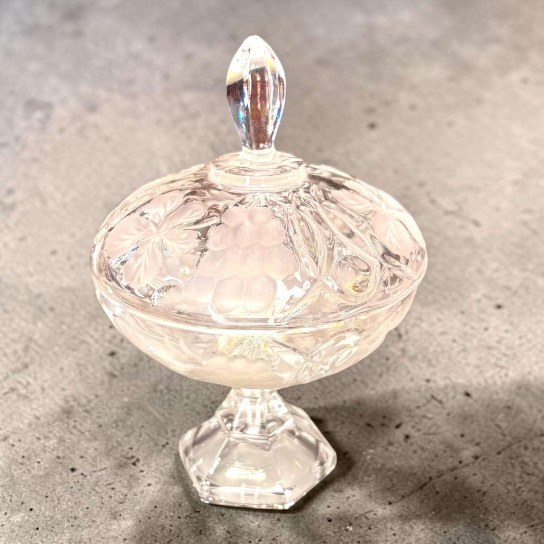 Bombonera antigua de cristal con relieves decorativos en forma de flores y uvas, con tapa y pie elevado, ideal para dulces o decoración vintage.