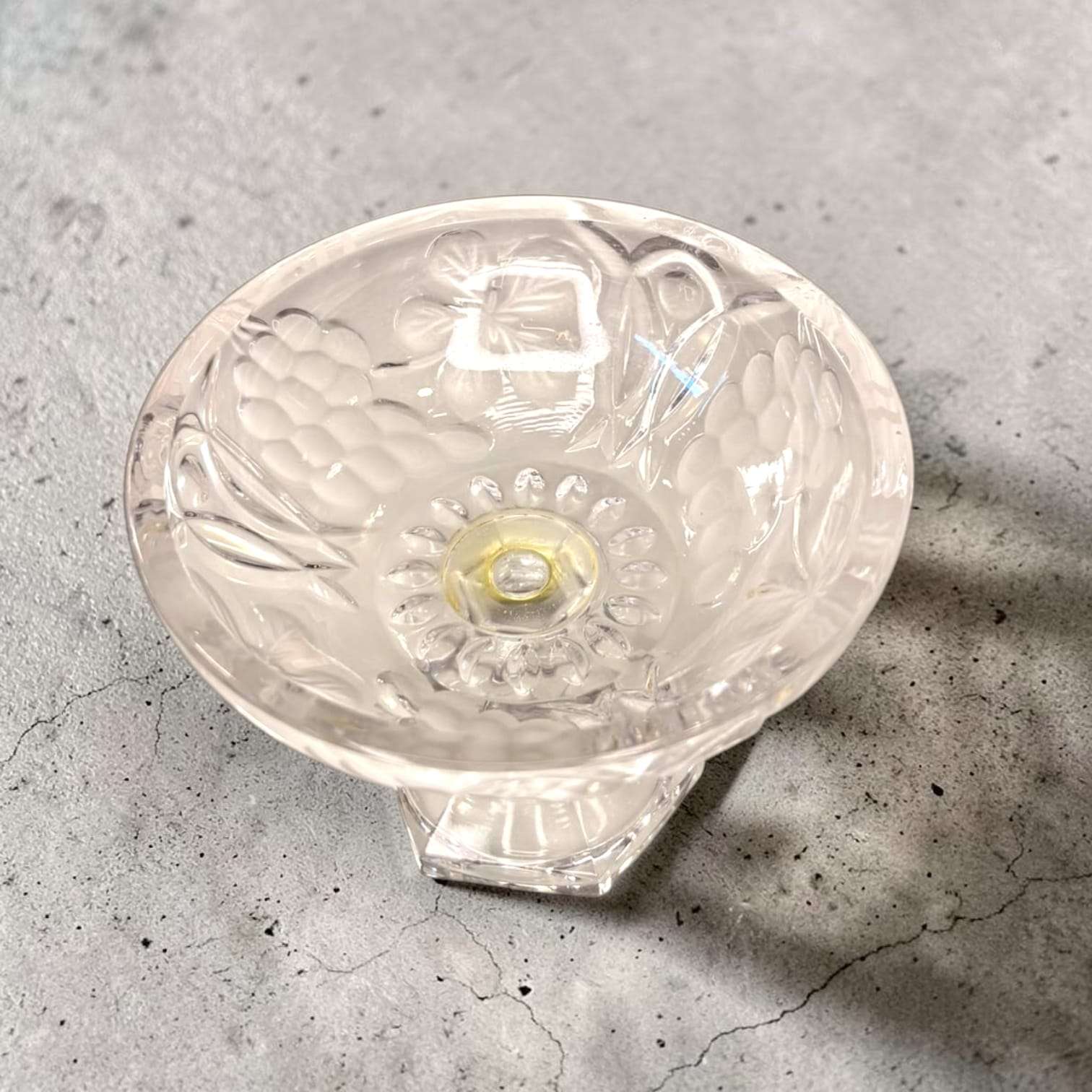 Base de la bombonera antigua de cristal con relieves florales y uvas, en forma de pedestal hexagonal, decorativa y elegante para colección.