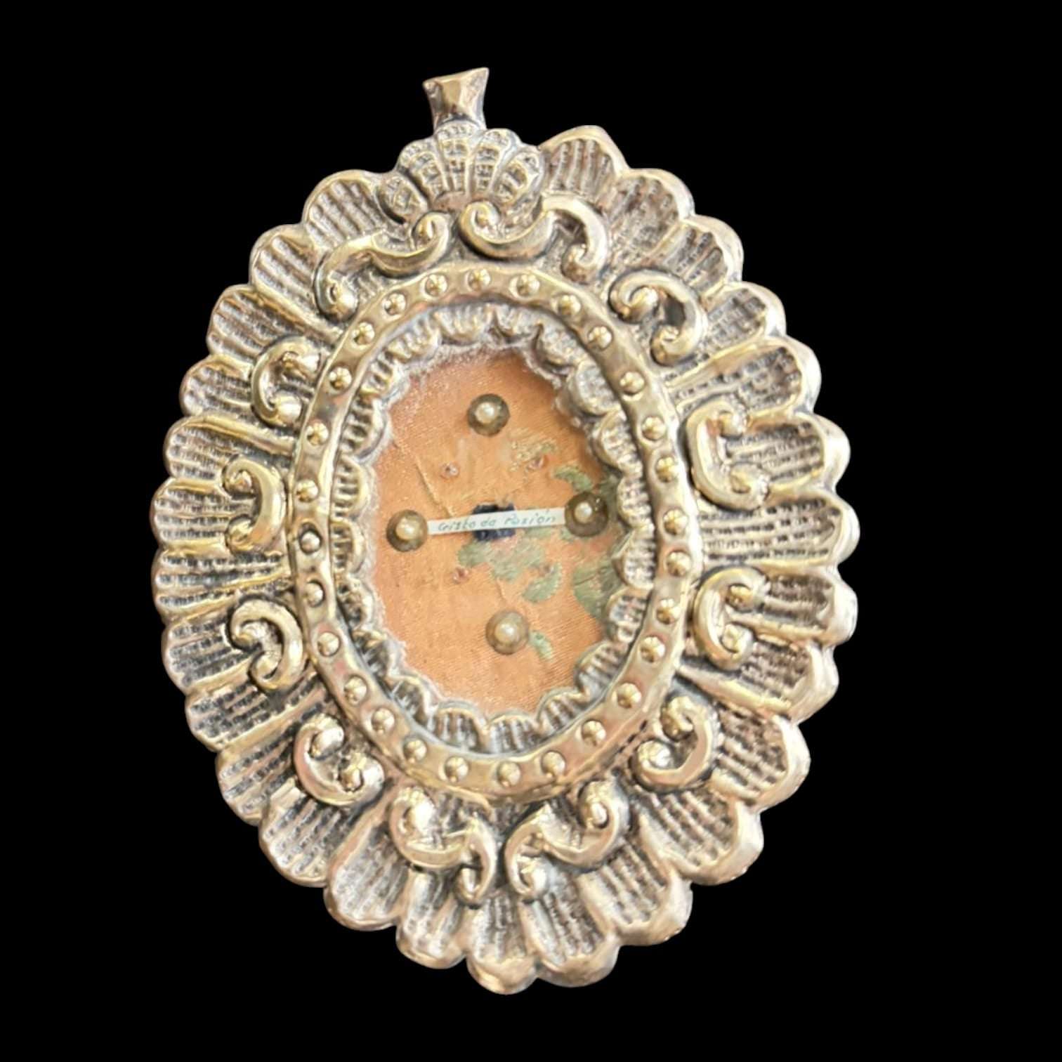 Relicario antiguo con fragmento de túnica bordada, marco decorativo en relieve con detalles dorados y perlas, pieza religiosa de colección.