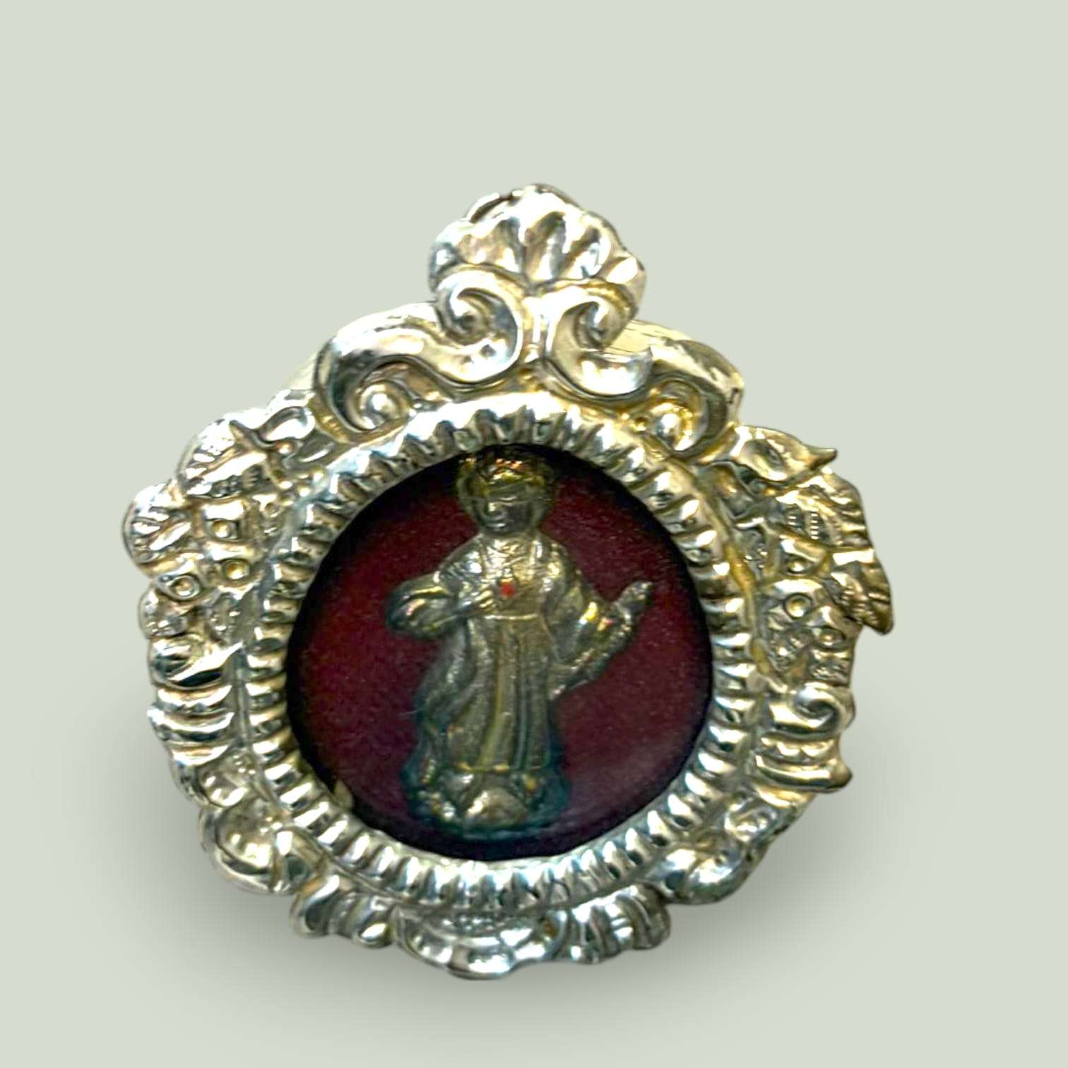 Relicario Niño Jesús en metal plateado con fondo de terciopelo rojo, vista frontal con detalles ornamentales en marco, SKU: A-138