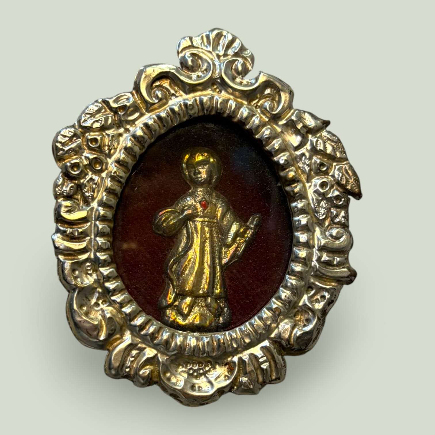 Detalle del relicario Niño Jesús en metal plateado, figura dorada en relieve sobre fondo de terciopelo rojo, SKU: A-138