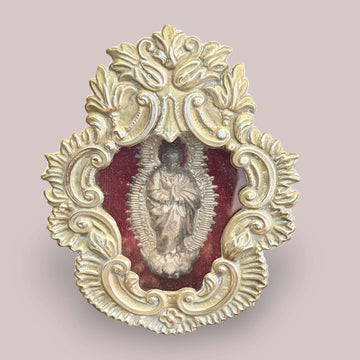 Relicario de la Inmaculada en metal plateado con fondo de terciopelo rojo, pieza religiosa antigua y decorativa, con detalles ornamentales elaborados.