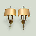 Apliques de pared en metal dorado con pantalla curva en color beige, con detalles en estilo clásico y estructura de soporte en metal dorado.