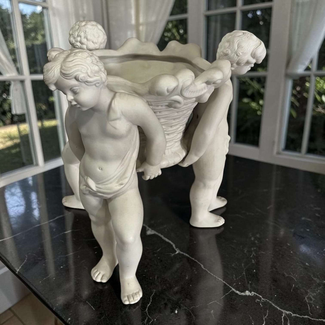 Centro de mesa de porcelana blanca con querubines sosteniendo una cesta, pieza clásica y elegante para decoración de mesas y vitrinas.