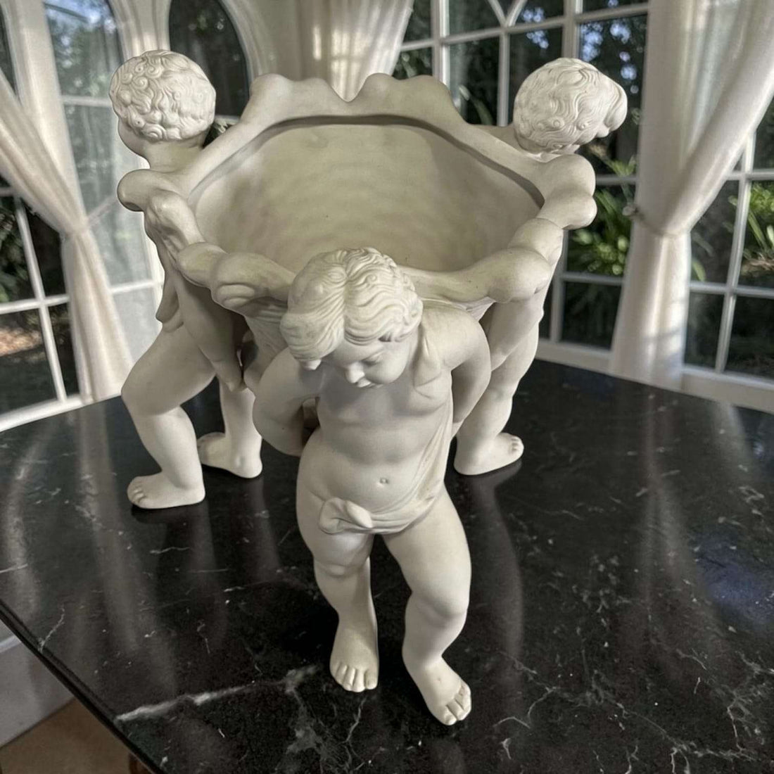 Centro de mesa de porcelana blanca con querubines sosteniendo una cesta, pieza clásica y elegante para decoración de mesas y vitrinas.