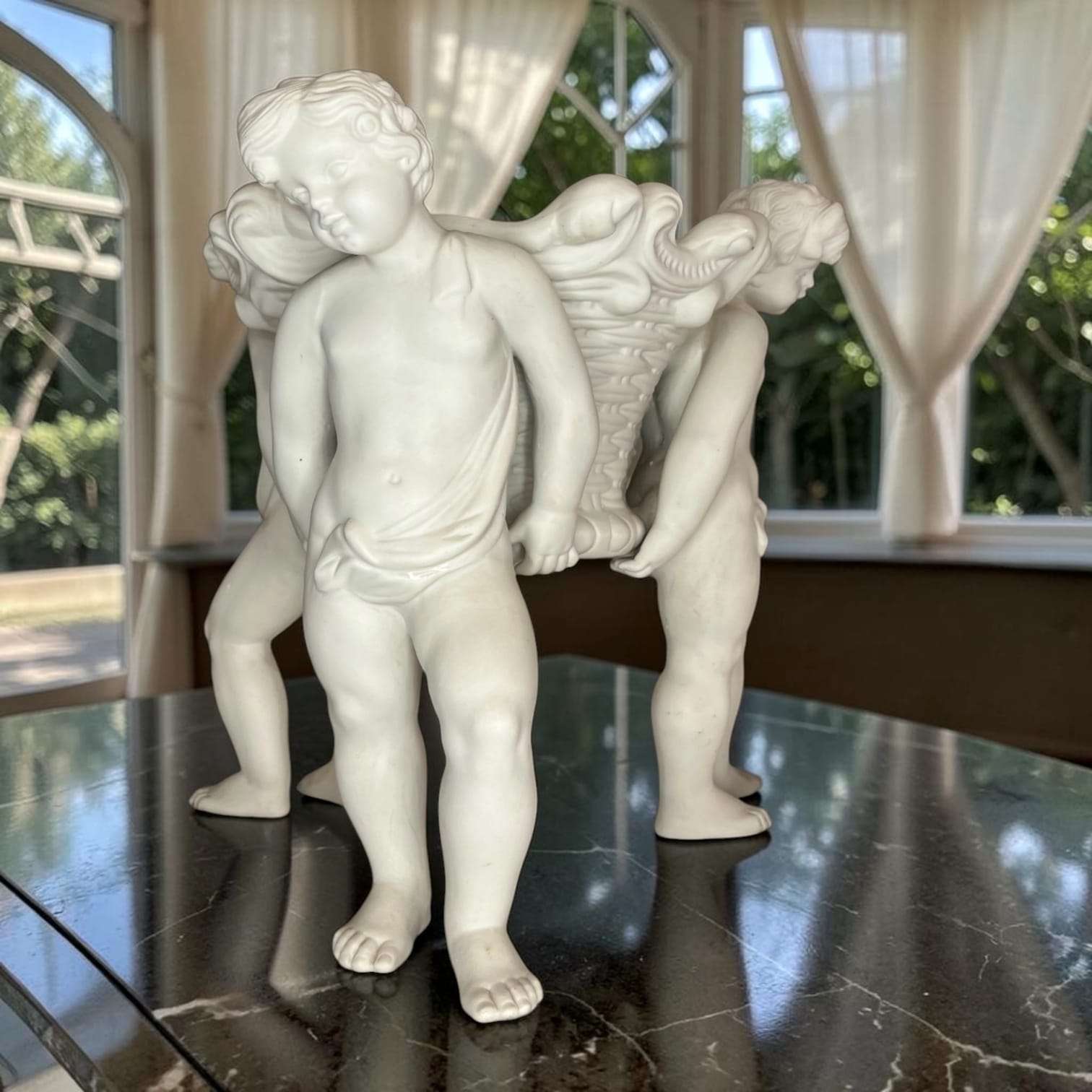 Perspectiva lateral del centro de mesa de porcelana con querubines, figura artística y decorativa para ambientes elegantes.