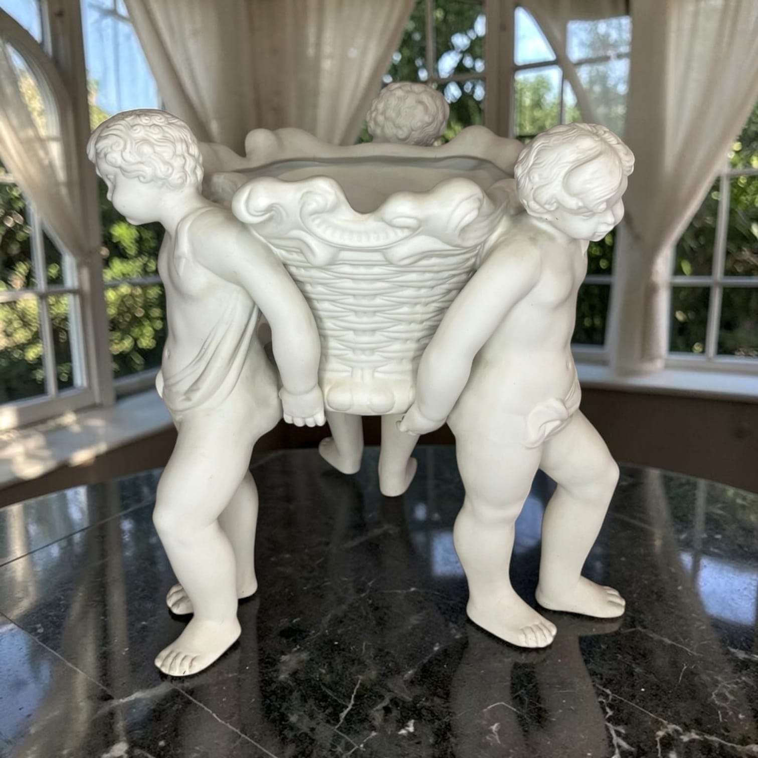 Detalle del rostro y cabello de los querubines en el centro de mesa de porcelana, pieza decorativa clásica para ambientes elegantes.