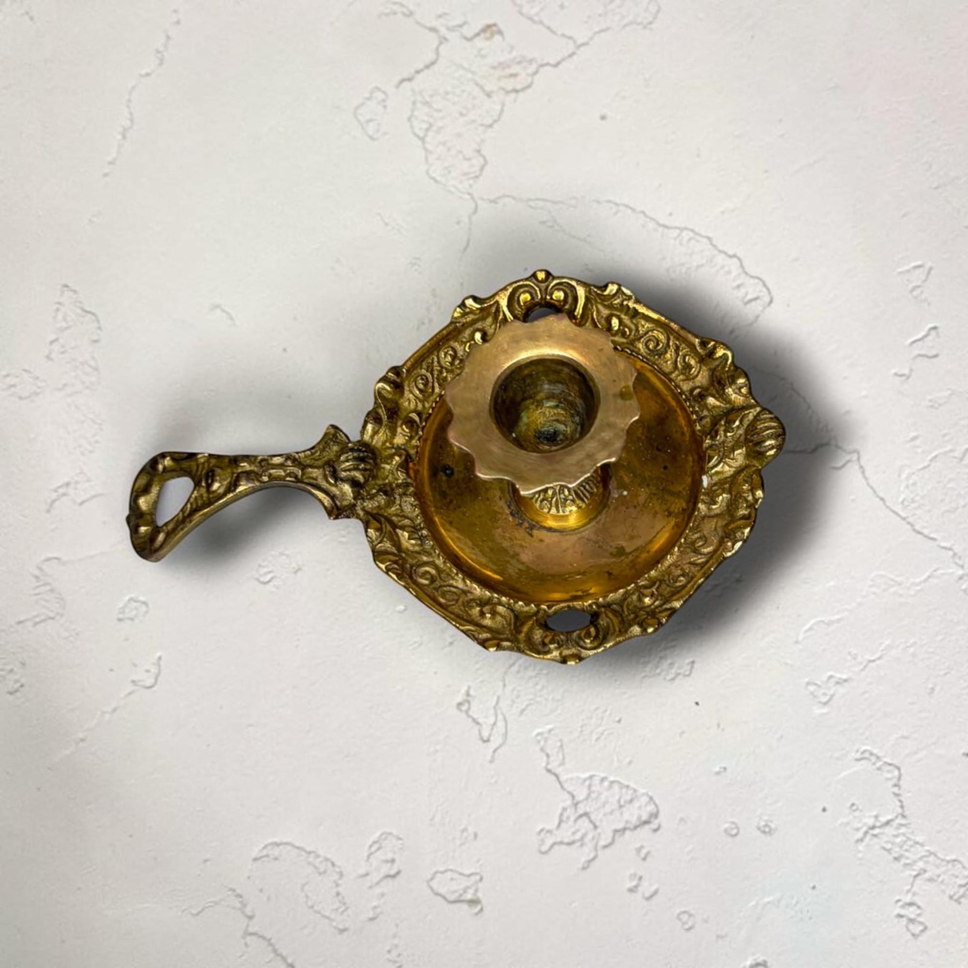 . El portavelas tiene un borde ondulado y un pequeño pedestal decorado. La pareja de palmatorias de metal dorado puede utilizarse hoy tanto con finalidad func