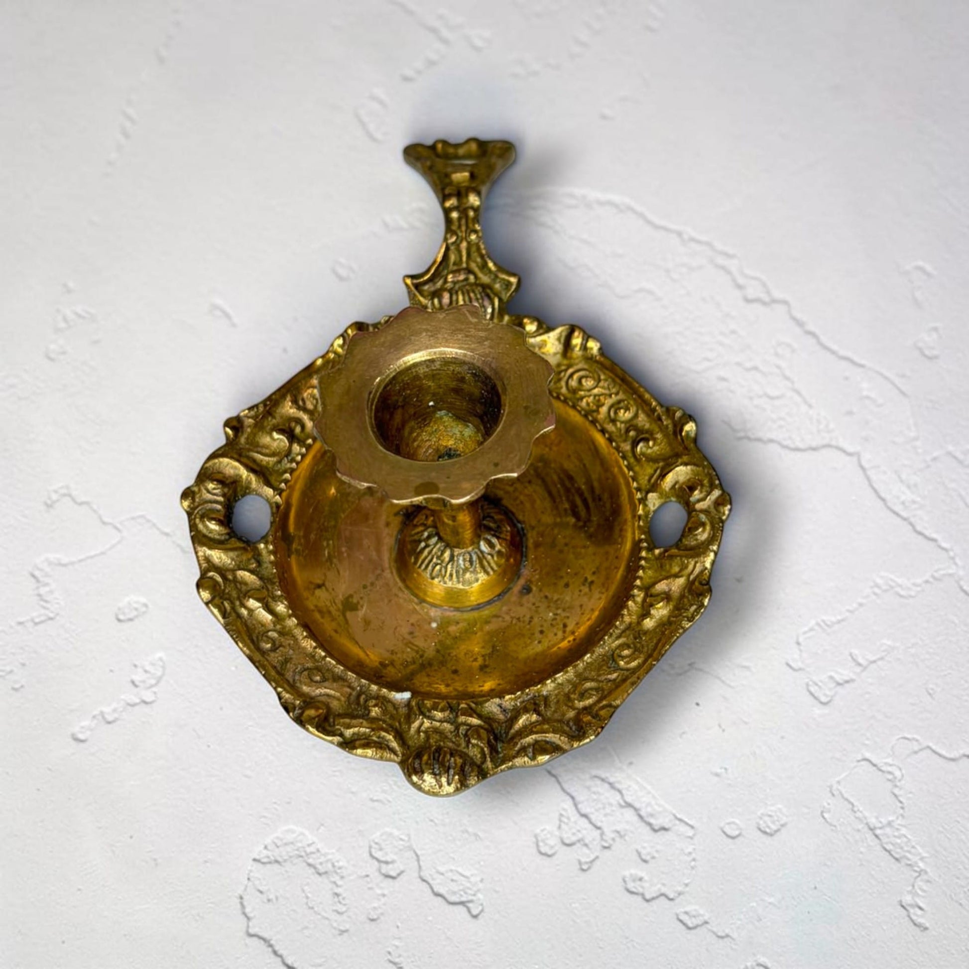 . El portavelas tiene un borde ondulado y un pequeño pedestal decorado. La pareja de palmatorias de metal dorado puede utilizarse hoy tanto con finalidad func
