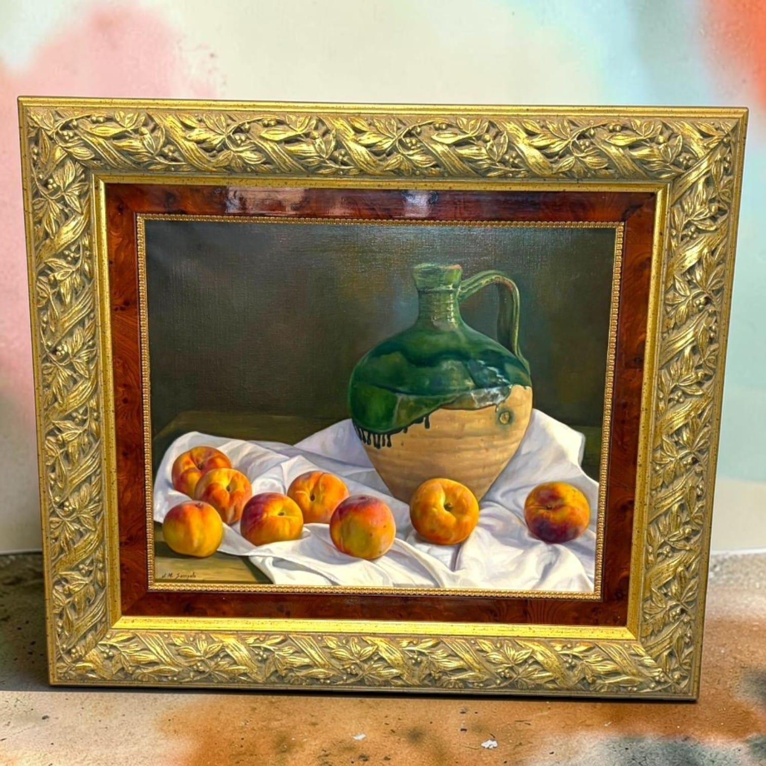 Este bodegón al óleo firmado J.M. Sampalo representa una composición de jarra y frutas sobre una tela blanca. 