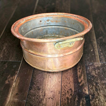 Este macetero antiguo de cobre presenta un formato ovalado y bajo