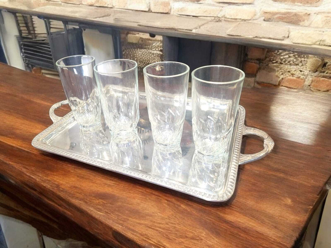 Juego de cuatro vasos de cristal tallado elegantes sobre bandeja de plata, perfectos para almuerzos especiales en decoración de mesa refinada.