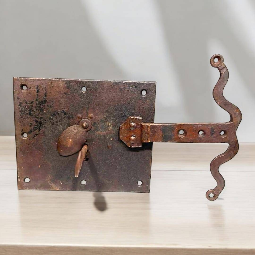 Cerradura antigua de hierro con llave montada sobre superficie clara, ideal para decoración rústica en el hogar. Diseño envejecido con estilo vintage.