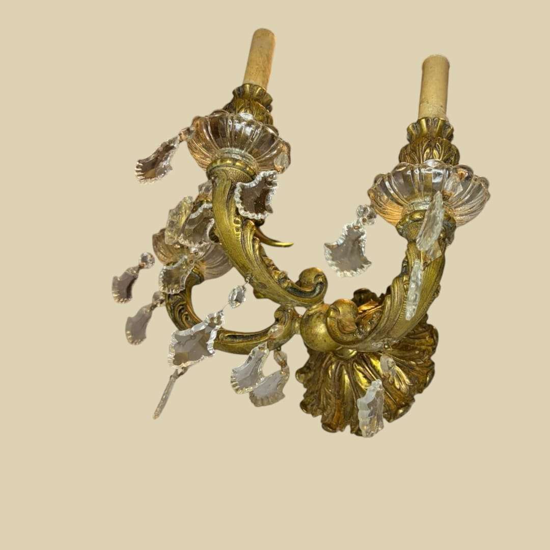 
Su estructura, de 32 cm de ancho, presenta tres brazos ornamentales en bronce envejecido, cuidadosamente moldeados con motivos vegetales y curvas arm