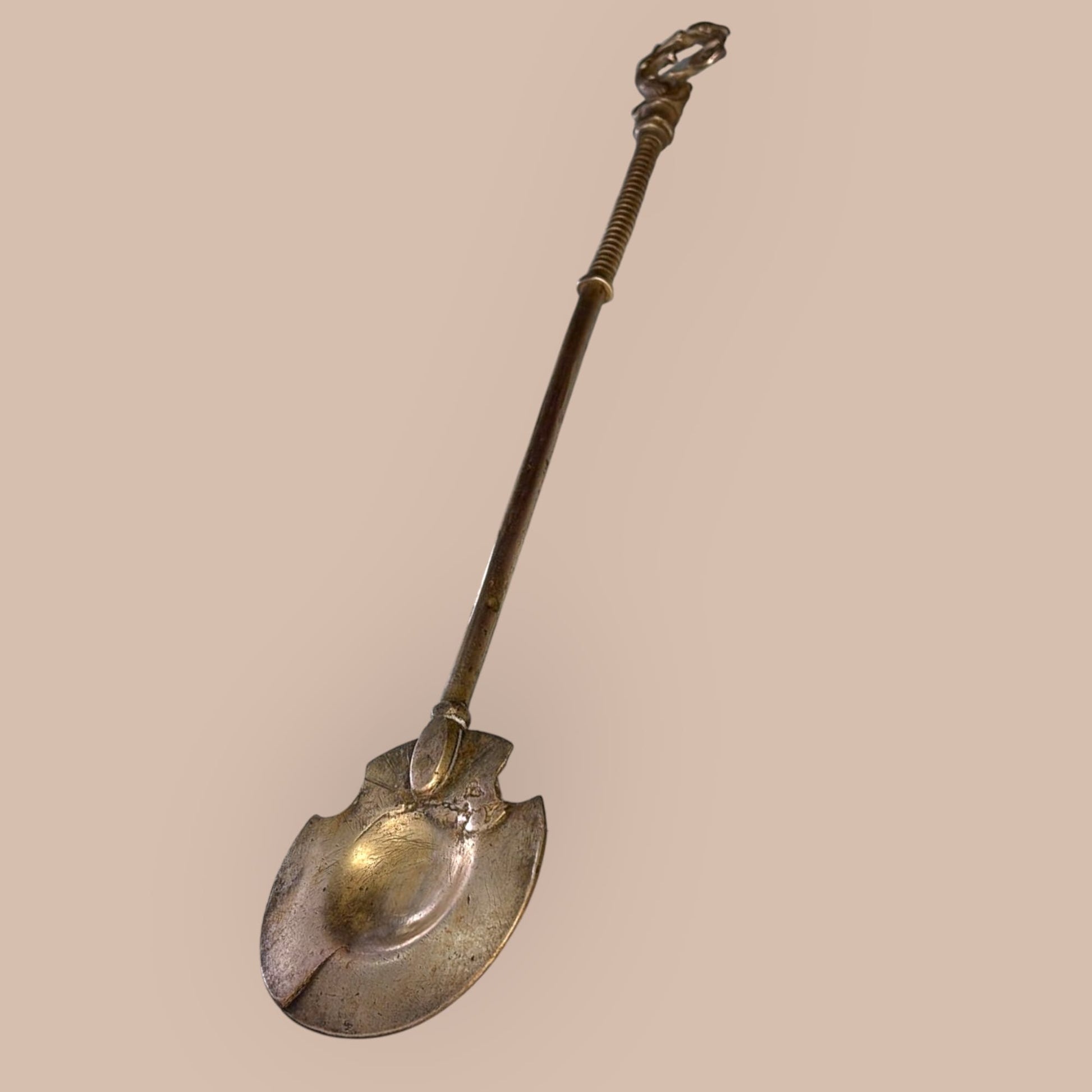 Badila de bronce antigua con forma cóncava y detalles artesanales, usada en braseros tradicionales como pieza funcional y decorativa de colección.