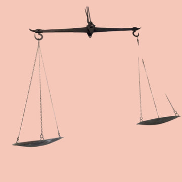 Vista frontal completa de la balanza antigua de hierro con sus platos metálicos suspendidos.