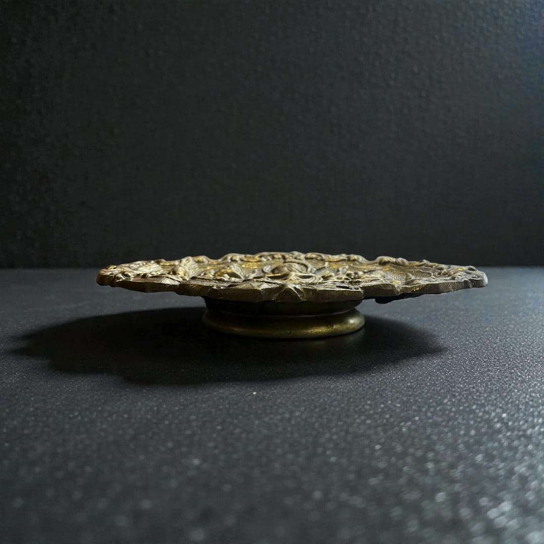 
Fabricada íntegramente en bronce macizo, esta Bandeja de bronce decorativa presenta una superficie ricamente trabajada con escenas figurativas en alto relieve, donde se aprecian personajes, e