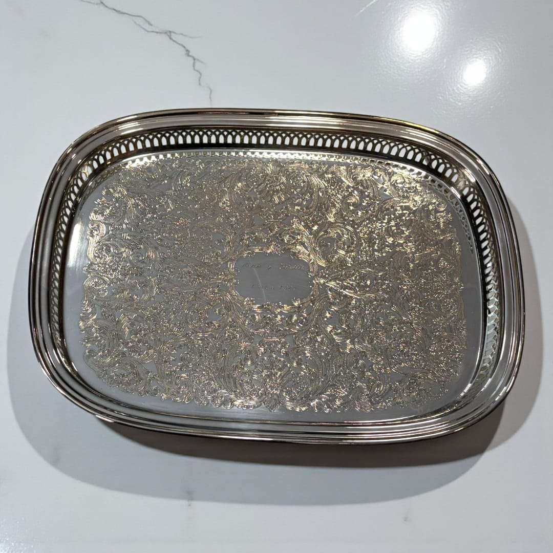 Bandeja de metal plateada grabada con bordes calados.
