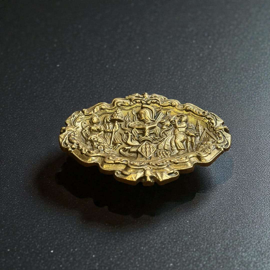
Fabricada íntegramente en bronce macizo, esta Bandeja de bronce decorativa presenta una superficie ricamente trabajada con escenas figurativas en alto relieve, donde se aprecian personajes, e