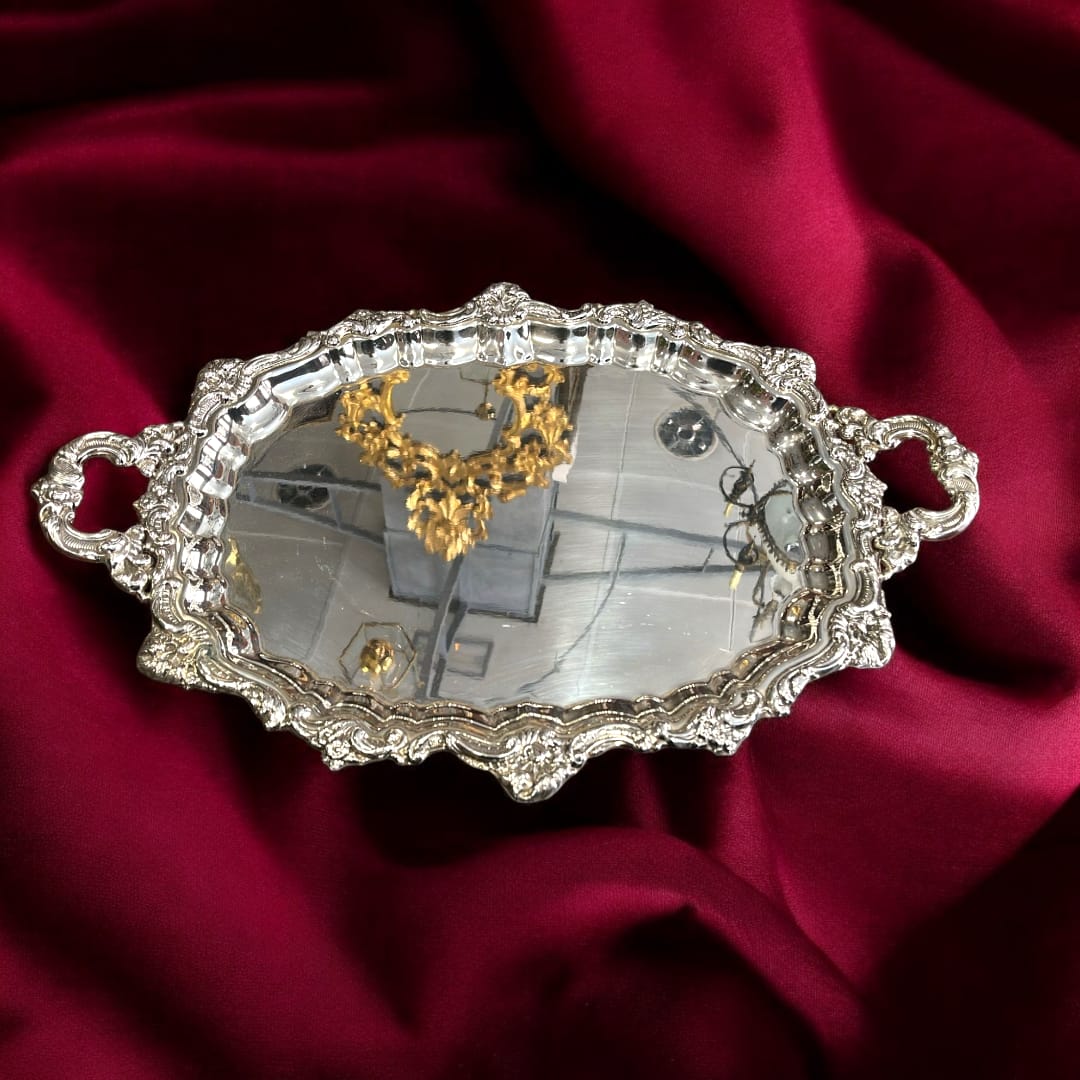 Bandeja de metal plateado estilo Luis XV con rocallas y asas ornamentales sobre tela roja. Ideal para decoración clásica.