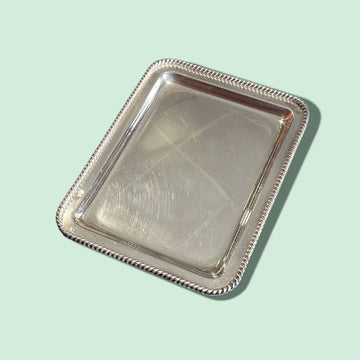 Bandeja de metal plateado con filo trenzado elegante, diseño rectangular vintage ideal para decoración en el hogar o uso funcional.