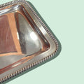 Detalle del borde trenzado repujado de la bandeja de metal plateado, estilo clásico perfecto para decoración sofisticada.