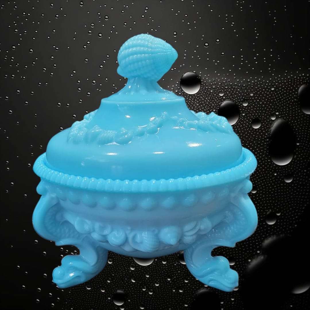 Bombonera de opalina azul con tapa y diseño vintage, decorada con relieve de conchas y base de tres patas curvas. Ideal para decoración elegante.