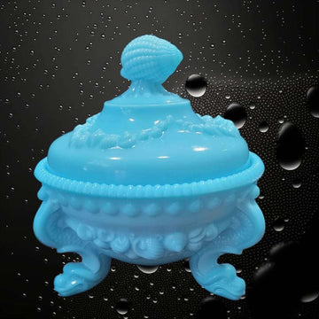 Bombonera de opalina azul con tapa y diseño vintage, decorada con relieve de conchas y base de tres patas curvas. Ideal para decoración elegante.